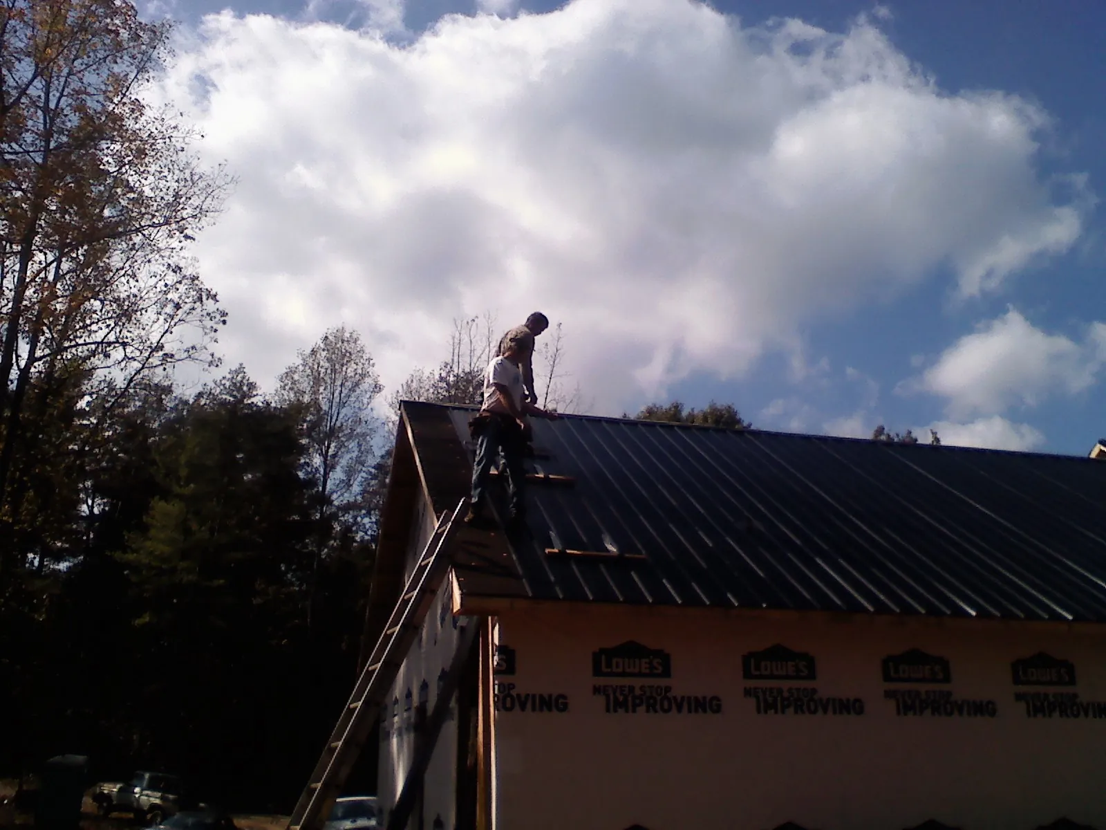 Roofer fastening dark metal panels high against a cloudy sky, from a Roof Inspection job in Troutville