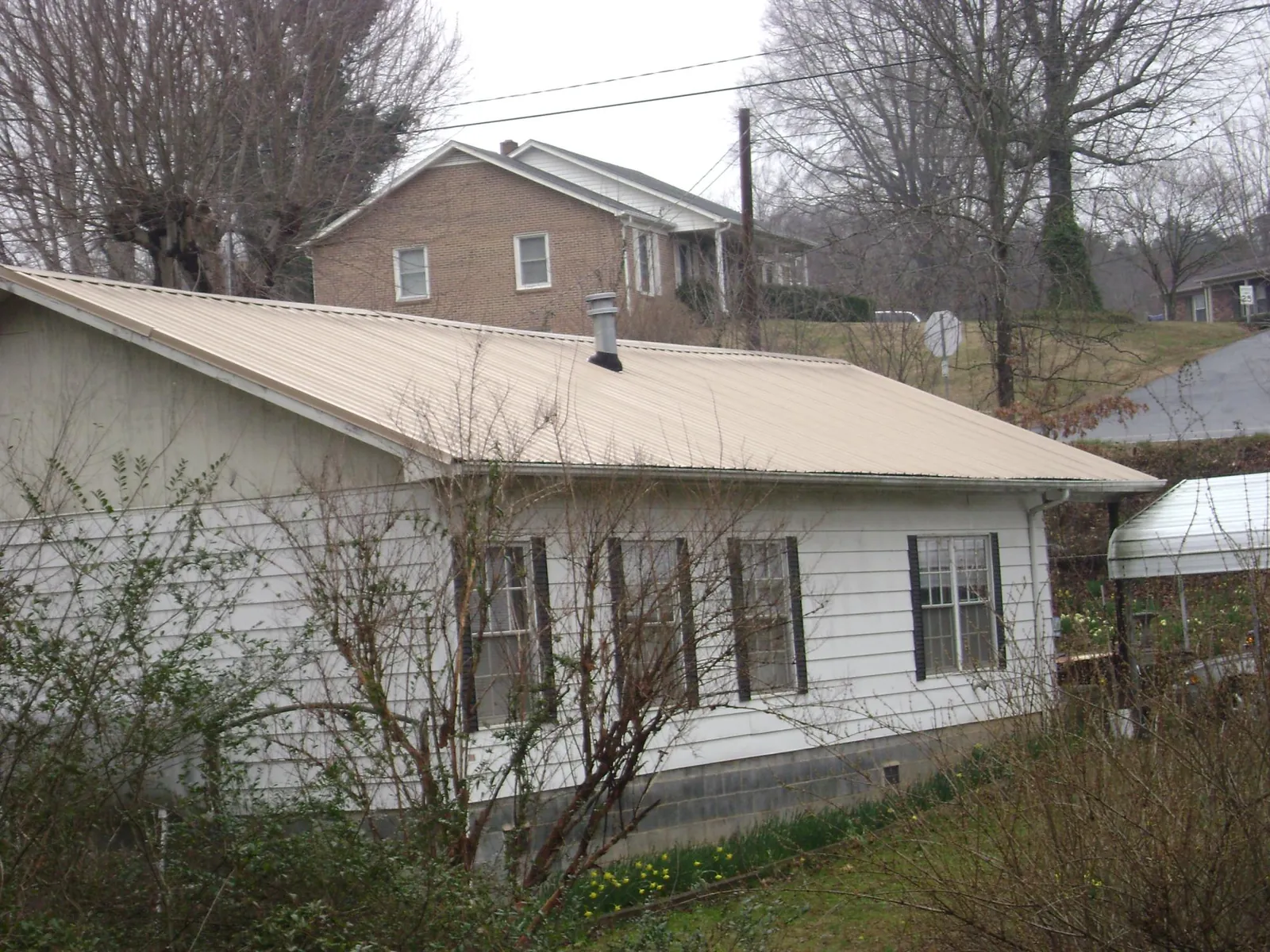 Tan metal roof on a white sided house set into a hillside — Commercial Roofing by Roofing Brothers in Troutville